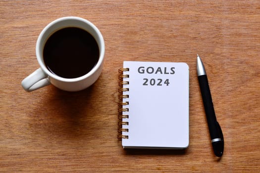 Goals 2024 text on notepad with coffee and pen on wooden desk. New Year's resolutions plan concept.