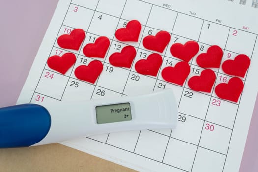 Positive pregnancy test with red heart shape on calendar. Trying To Conceive Concept.