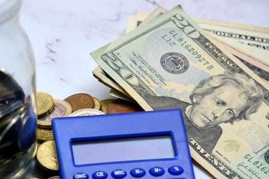 Glass jar with multicurrency coins, US dollar bills and calculator white table. Saving and travelling concept