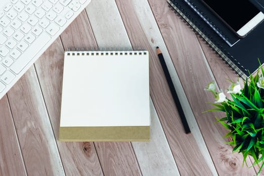 Directly above view of office desk with white computer keyboard, pen, smartphone, notepad and potted plant.