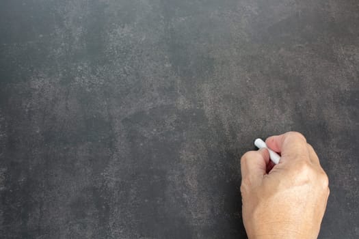 Male hand writes in white chalk pencil on a chalkboard background. Copy space. Teaching concept.