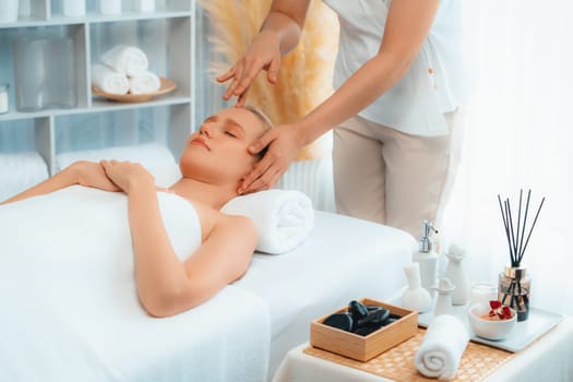 Caucasian woman enjoying relaxing anti-stress head massage and pampering facial beauty skin recreation leisure in dayspa modern light ambient at luxury resort or hotel spa salon. Quiescent