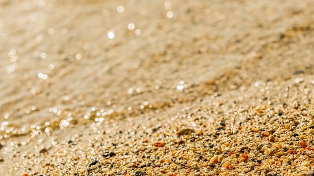 A background of sand, small pebbles and flowing waves on the sea beach. Summer vacation and coastal nature concept