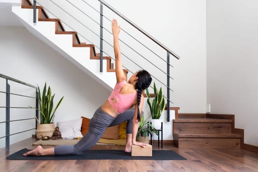 Young woman doing yoga twist at home using cork yoga block. Copy space. Wellness and spirituality concept.