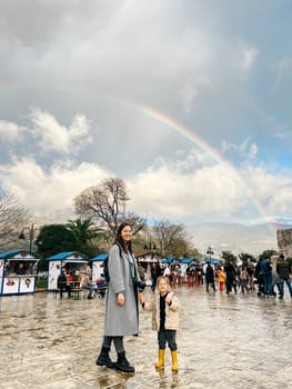 Mom with a little girl are standing near the market against the backdrop of a rainbow over the mountains. High quality photo