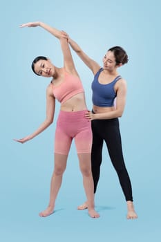 Asian woman in sportswear doing yoga exercise in standing pose with her trainer or yoga buddy. Healthy body care and meditation yoga lifestyle in full shot on isolated background. Vigorous