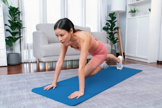 Asian woman in sportswear doing burpee on exercising mat as home workout training routine. Attractive girl engage in her pursuit of healthy lifestyle and fit body physique. Vigorous