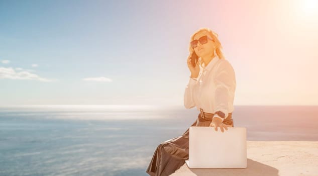 Business woman on nature in white shirt and black skirt. She works with an iPad in the open air with a beautiful view of the sea. The concept of remote work