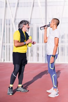 vertical photo of a senior sports man drinking water with his personal trainer before training, concept of healthy and active lifestyle in middle age