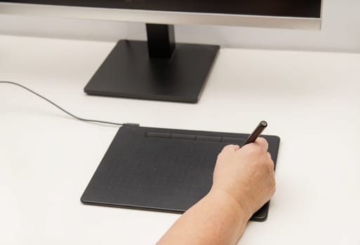 Woman hand working on her computer with a digital graphic tablet, in the background a monitor with an image