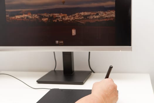 Woman hand working on her computer with a digital graphic tablet, in the background a monitor with an image