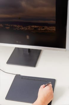 Woman hand working on her computer with a digital graphic tablet, in the background a monitor with an image