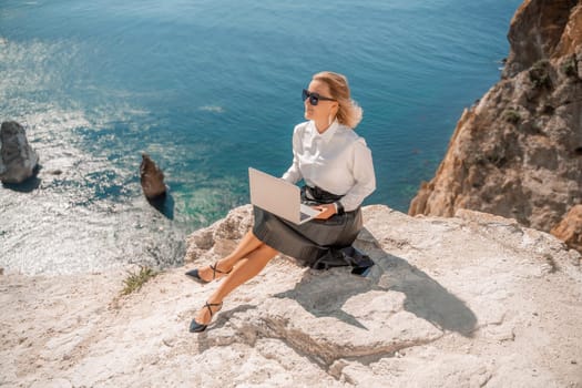 Business woman on nature in white shirt and black skirt. She works with an iPad in the open air with a beautiful view of the sea. The concept of remote work