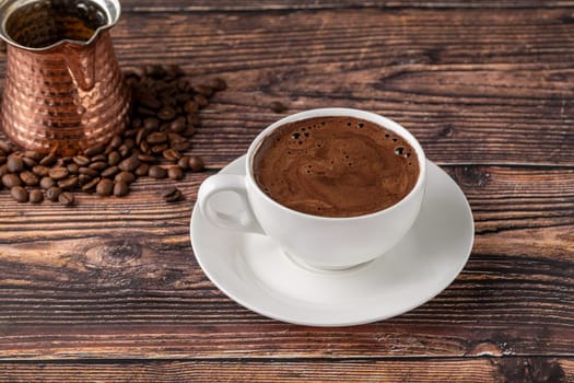 Double Turkish coffee in a white porcelain cup with a decorative coffee pot on a wooden table