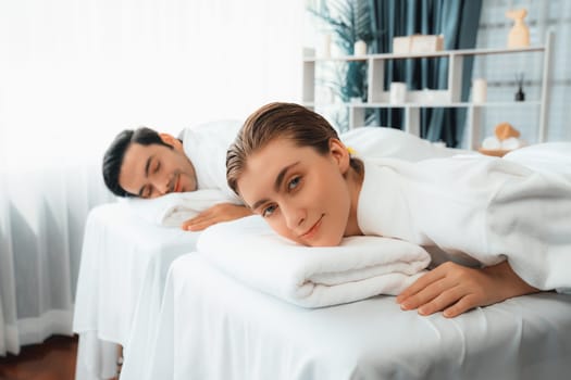 Caucasian couple customer enjoying relaxing anti-stress spa massage and pampering with beauty skin recreation leisure in day light ambient salon spa at luxury resort or hotel. Quiescent