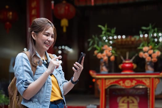 Happy young Asian tourist woman using smartphone on street with market background, Female traveller enjoy shopping market during holidays.