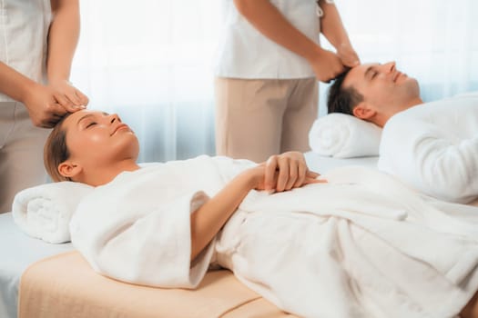 Caucasian couple enjoying relaxing anti-stress head massage and pampering facial beauty skin recreation leisure in dayspa modern light ambient at luxury resort or hotel spa salon. Quiescent