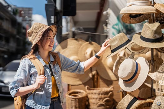 Happy young woman asian is visit local market during her trip and purchase straw hat handmade. Tourist women travel enjoy shopping market during holidays, backpacker traveller.