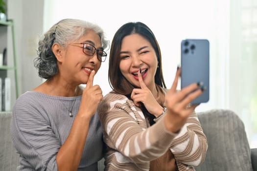 Happy young Asian woman taking selfie picture on smartphone with happy mature mother.