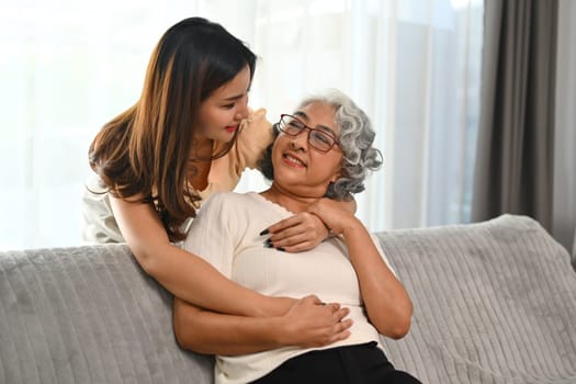 Smiling Adult daughter standing behind couch and embracing older mother. Family bonding concept.