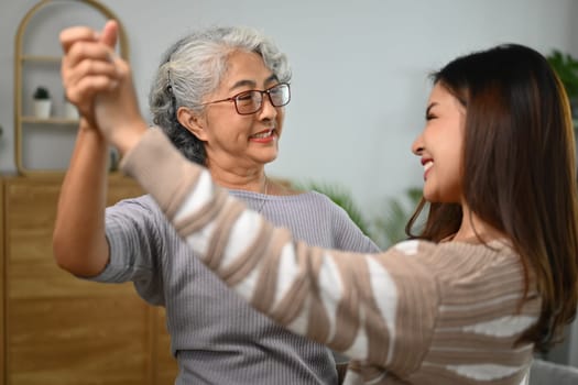 Happy gray haired middle age mother dancing with grown up daughter in living room.