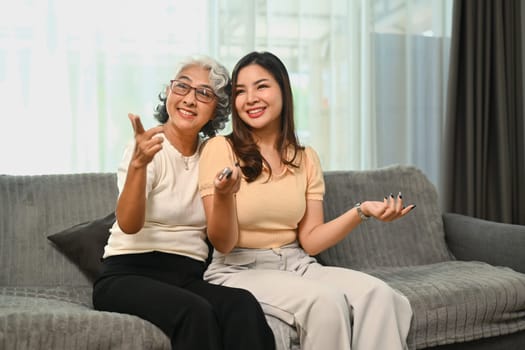 Cheerful retired woman relaxing on sofa with grown up daughter and watching tv on weekend.