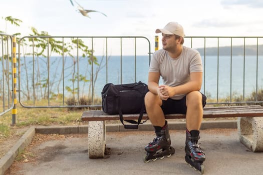 Portrait of happy handsome male roller in inline roller skates sitting on bench on the park