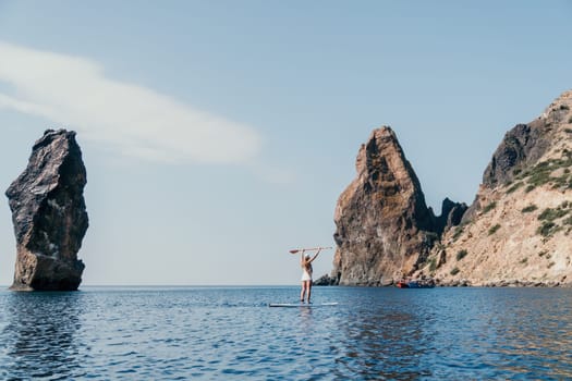 Close up shot of beautiful young caucasian woman with black hair and freckles looking at camera and smiling. Cute woman portrait in a pink bikini posing on a volcanic rock high above the sea