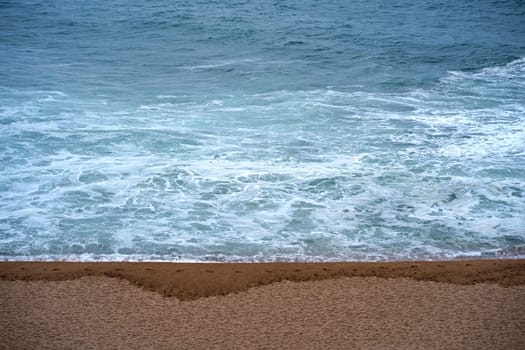 Top view over the sea beach. Beautiful sea waves. Sandy beach and stunning sea. Summer sunset seascape. Water texture. Human footprints on wet sand.