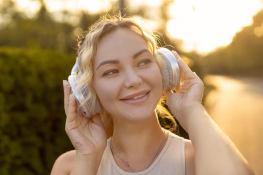 Portrait of fit girl preparing for running in workout clothes looking at camera smiling. Beautiful happy sportswoman enjoying doing sports listening to music using headphones. Music concept