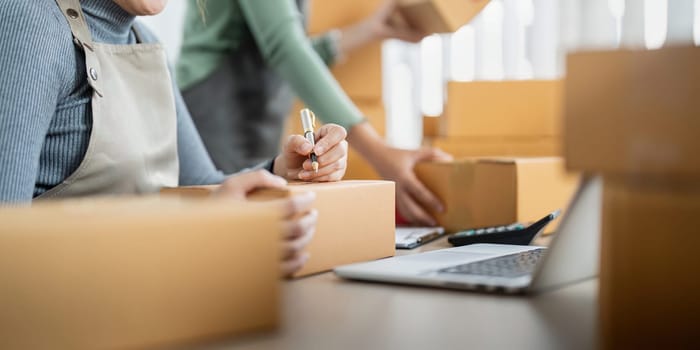 Startup small business owner working with computer at workplace. Two woman seller check product order. Packing goods for delivery to customer. Online selling. Ecommerce. Online Shopping.