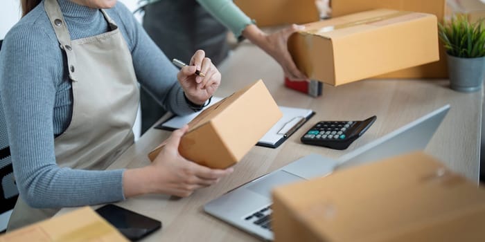 Startup small business owner working with computer at workplace. Two woman seller check product order. Packing goods for delivery to customer. Online selling. Ecommerce. Online Shopping.