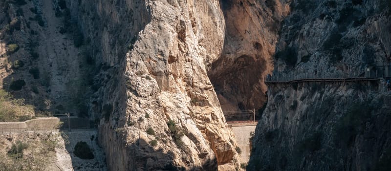 Scenic view of Caminito del Rey with tourists on walkways and a train passing through the canyon in Malaga.