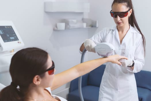 Woman in a beauty salon removes hair from her arm with laser epilation