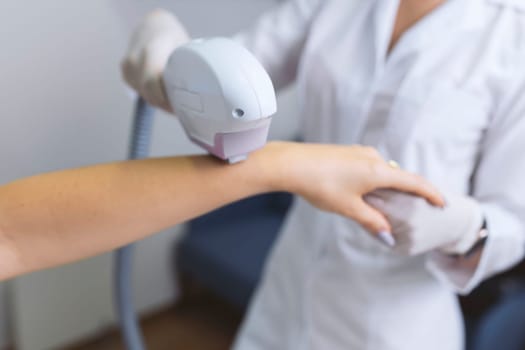 Woman in a beauty salon removes hair from her arm with laser epilation