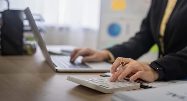 Businesswoman accountant using calculator and laptop for financial data saving in office room, Business financial, tax, accounting concept.