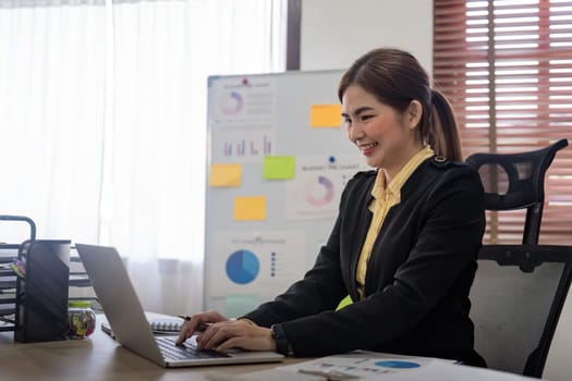 Young asian businesswoman sitting at desk with data and graph by using calculator finance accounting analyze, plan, and strategy about business improvement.