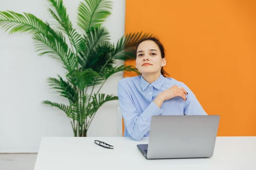 Image of young pleased happy cheerful cute beautiful business woman sit indoors in office using laptop computer listening music with earphones.