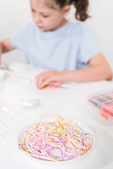 Little girl enjoys crafting colorful bracelets with vibrant clay beads set.