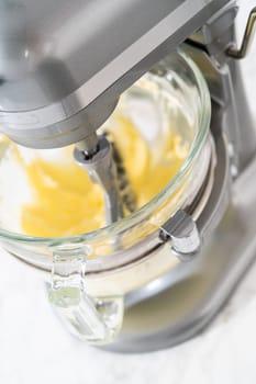 Whisking buttercream frosting in a glass mixing bowl with an electric kitchen mixer for American flag mini cupcakes.