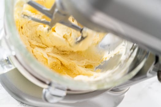 Whisking buttercream frosting in a glass mixing bowl with an electric kitchen mixer for American flag mini cupcakes.