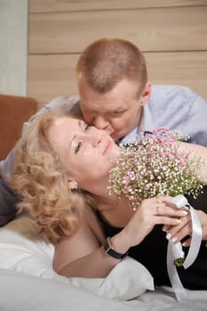 Loving enamored adult couple communicates, embraces, and has fun alone together on the bed in the bedroom or hotel room. The woman is wearing tank top and the man is shirtless