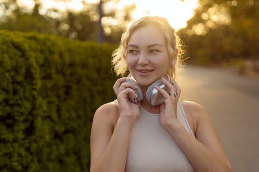 Portrait of fit girl preparing for running in workout clothes looking at camera smiling. Beautiful happy sportswoman enjoying doing sports listening to music using headphones. Music concept