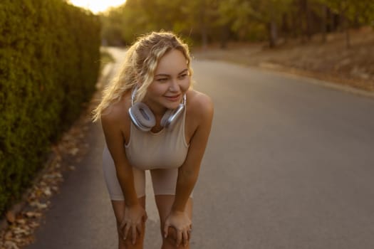 Portrait of fit girl preparing for running in workout clothes looking at camera smiling. Beautiful happy sportswoman enjoying doing sports listening to music using headphones. Music concept