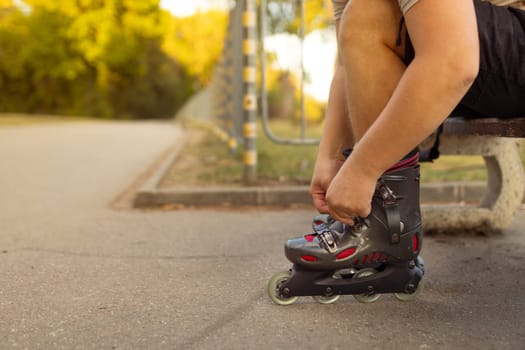 Legs of young man putting on roller skates in the park.