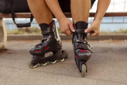 Legs of young man putting on roller skates in the park.