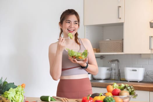 Healthy Asian woman takes care of her health by eating vegetable and fruit salad, adding vitamins in the kitchen..