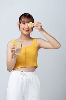 young woman holding lemon slice in front of eye