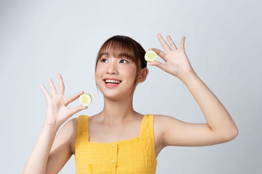 A picture of a face of a beautiful woman posing with a cucumber over white background