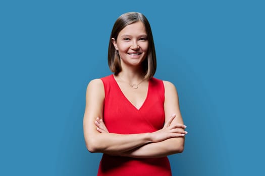 Portrait of young happy laughing confident woman in red on blue studio background. Successful fashionable female with crossed arms looking at camera. Beauty fashion professions and services